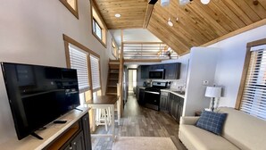 A modern interior with a flat-screen TV, a sofa, a kitchen area, and a staircase leading to an upper level.