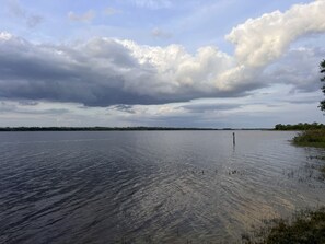 Rustig wateroppervlak met een verre oever, bewolkte lucht en een eenzame paal in het water.