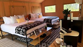 A tent with two beds, a small table, a refrigerator, and a window.