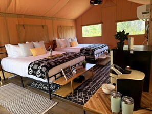 A tent with two beds, a small table, a refrigerator, and a window.