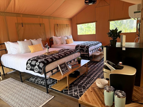 A tent with two beds, a small table, a refrigerator, and a window.