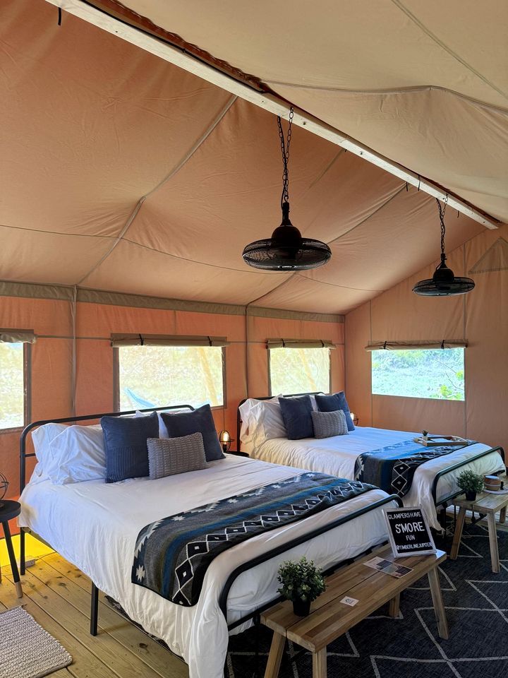 A tented accommodation with two beds, a hanging light fixture, and a sign on the bench.