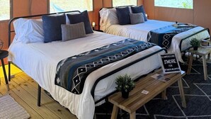 A tented accommodation with two beds, a hanging light fixture, and a sign on the bench.