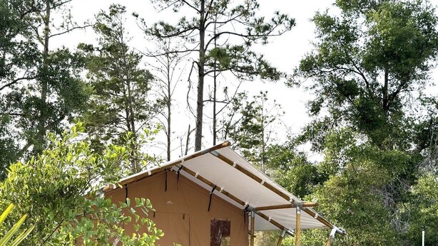 A small, single-story cabin with a pitched roof, surrounded by dense trees.
