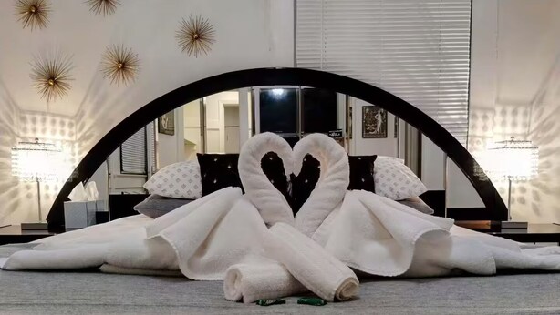 Ein Bett mit Handtüchern, die zu einem Herzen geformt sind, ein Spiegel darüber und Wandleuchten.