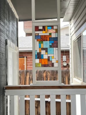 A window with a colorful stained glass design, a wooden fence, and a brick wall in the background. - Deco Studio Retreat: Fireplace, WiFi, Queen Bed (Reno)