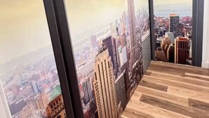 Ein Zimmer mit einer großen Stadtkulissen-Mural, Holzboden und einem Fenster mit schwarzem Rahmen.