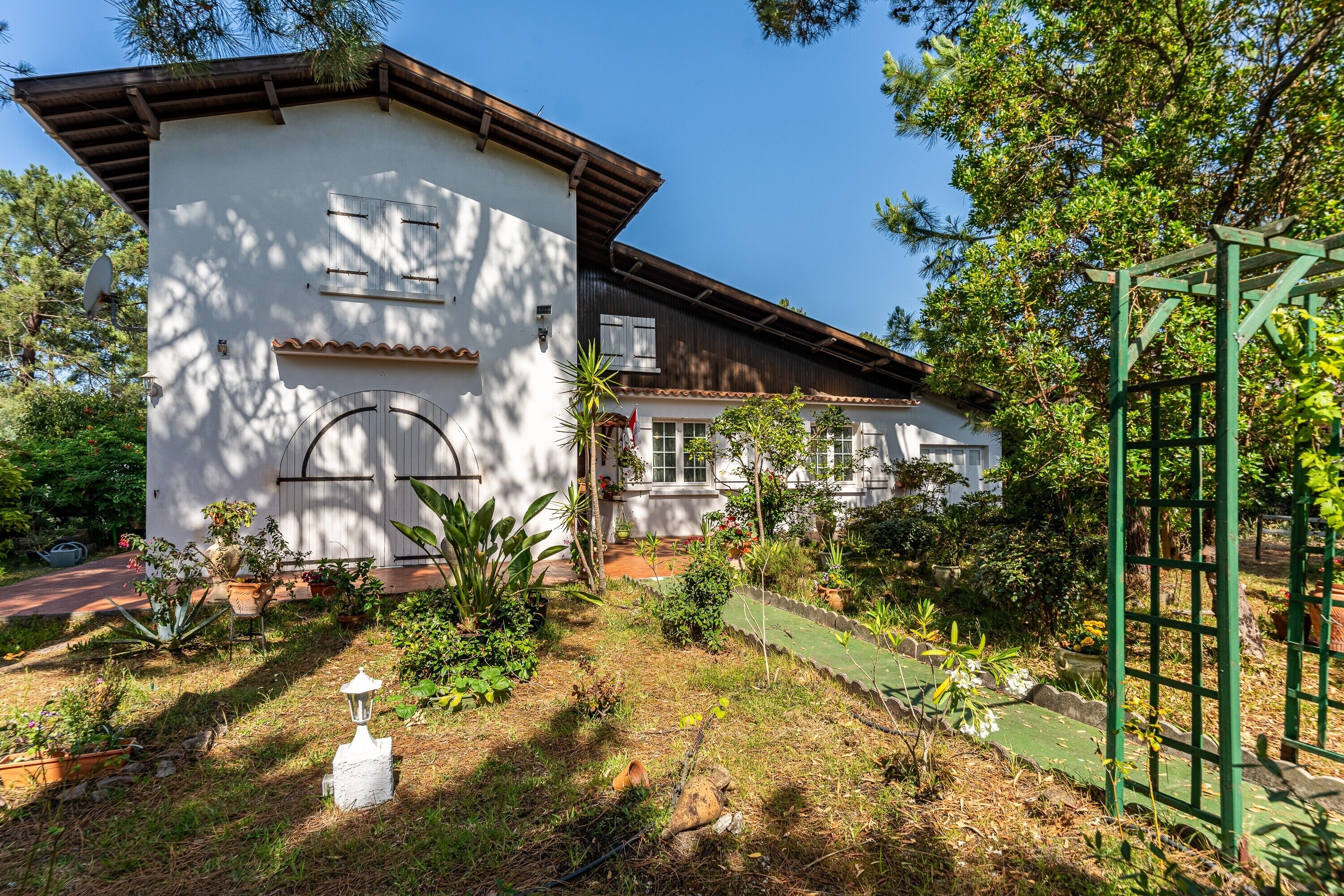 Ein zweistöckiges Gebäude mit weißer Fassade, einem Ziegeldach und einem kleinen Gartenbereich mit verschiedenen Pflanzen und einem Weg.