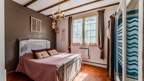 Une chambre avec un lit en bois, un radiateur, une fenêtre avec des rideaux et une vue sur l’extérieur.