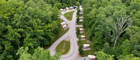 An aerial view of a campsite with a gravel road, RVs, and several tent-style cabins.