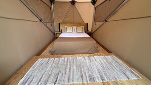 A tented room with a bed, a wooden floor, and a patterned rug.