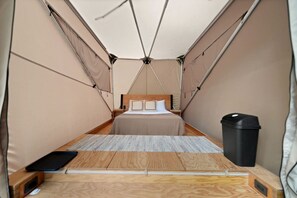 A compact tent with a bed, a small table, and a trash bin.