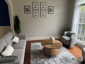Ein Wohnzimmer mit grauem Sofa, einem runden Couchtisch aus Holz und einem grauen, flauschigen Teppich.
