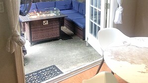 A room with a wooden floor, a white chair, a table, and a view through a glass door to an outdoor seating area with a blue sofa and a barbecue grill. - Welcome to Atlanta: Old-Fashion Charm Meets Modern Retreat Near Airport (Atlanta)