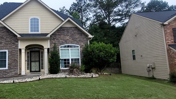 A two-story house with a stone facade, a front door, and a small front yard with a tree and a rock garden. - Welcome to Atlanta: Old-Fashion Charm Meets Modern Retreat Near Airport (Atlanta)
