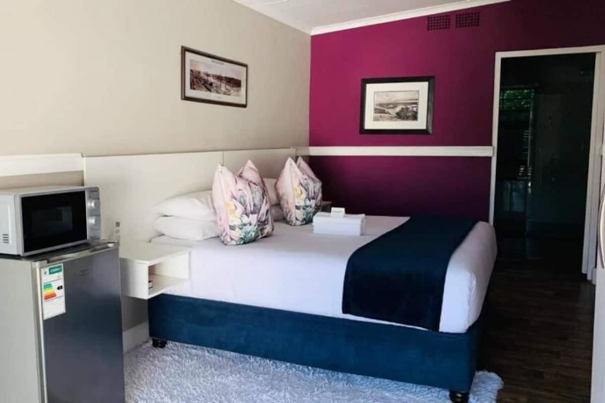 A hotel room with a bed, a microwave, a small refrigerator, and a door leading to a balcony.
