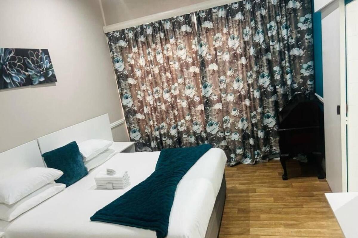 A hotel room with a bed, a desk, a chair, a curtain, and a painting on the wall.