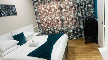 Une chambre d’hôtel avec un lit, un bureau, une chaise, un rideau et un tableau au mur.