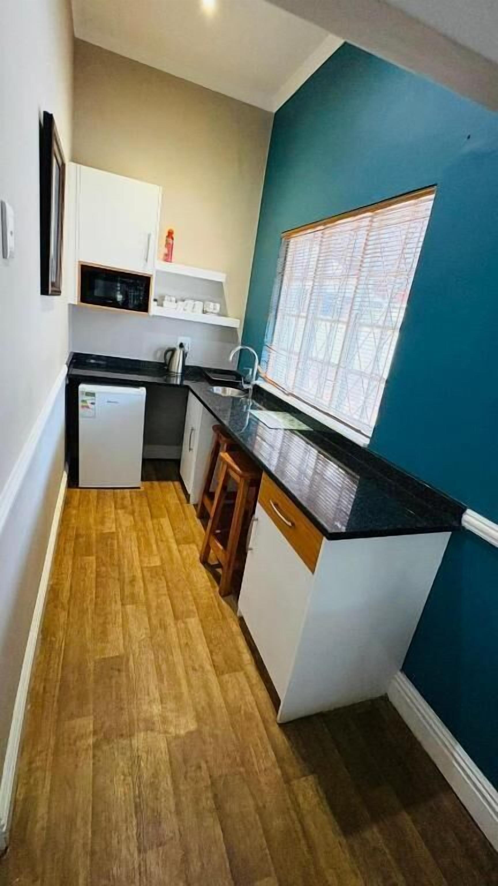 A compact kitchen with a refrigerator, sink, and wooden flooring.