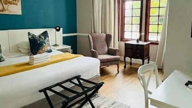 Quarto com cama, escrivaninha, cadeira e janela com cortinas.