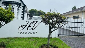 Um edifício branco com telhado preto e uma placa com a inscrição 'Hidden Villas Guesthouse'.
