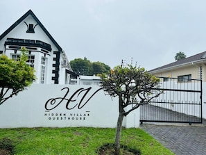 Un edificio blanco con techo negro y un cartel que dice 'Hidden Villas Guesthouse'.