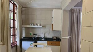 Cozinha compacta com mesa branca, bancada preta e armário branco sobre a pia.