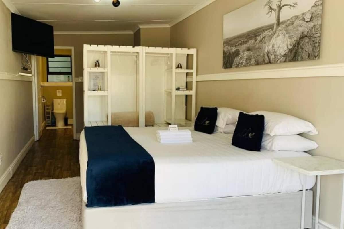 A bedroom with a bed, bedside tables, a white wall, a painting, and a wardrobe.