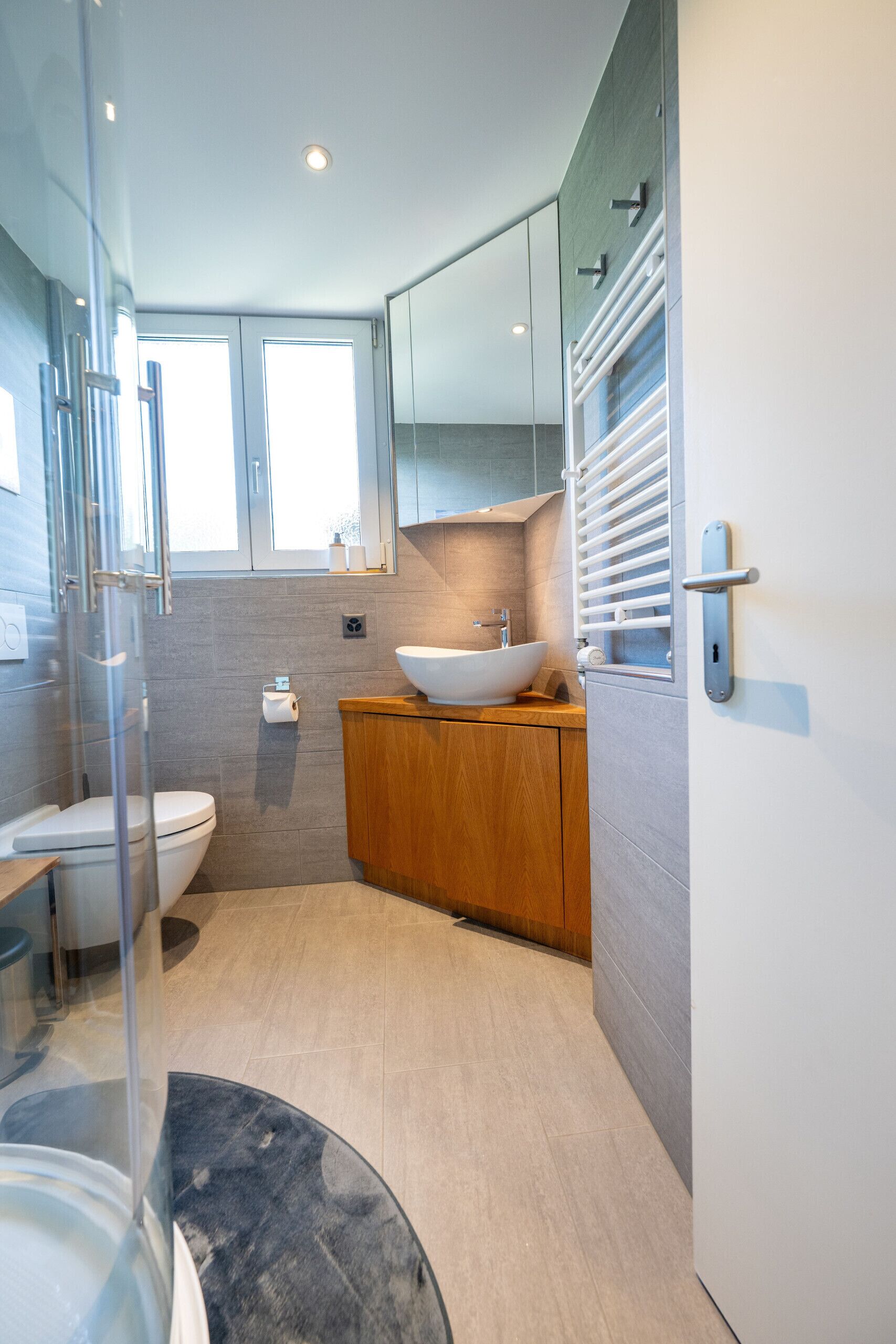 A modern bathroom with a glass shower enclosure, a wooden vanity, a white sink, and a large mirror.