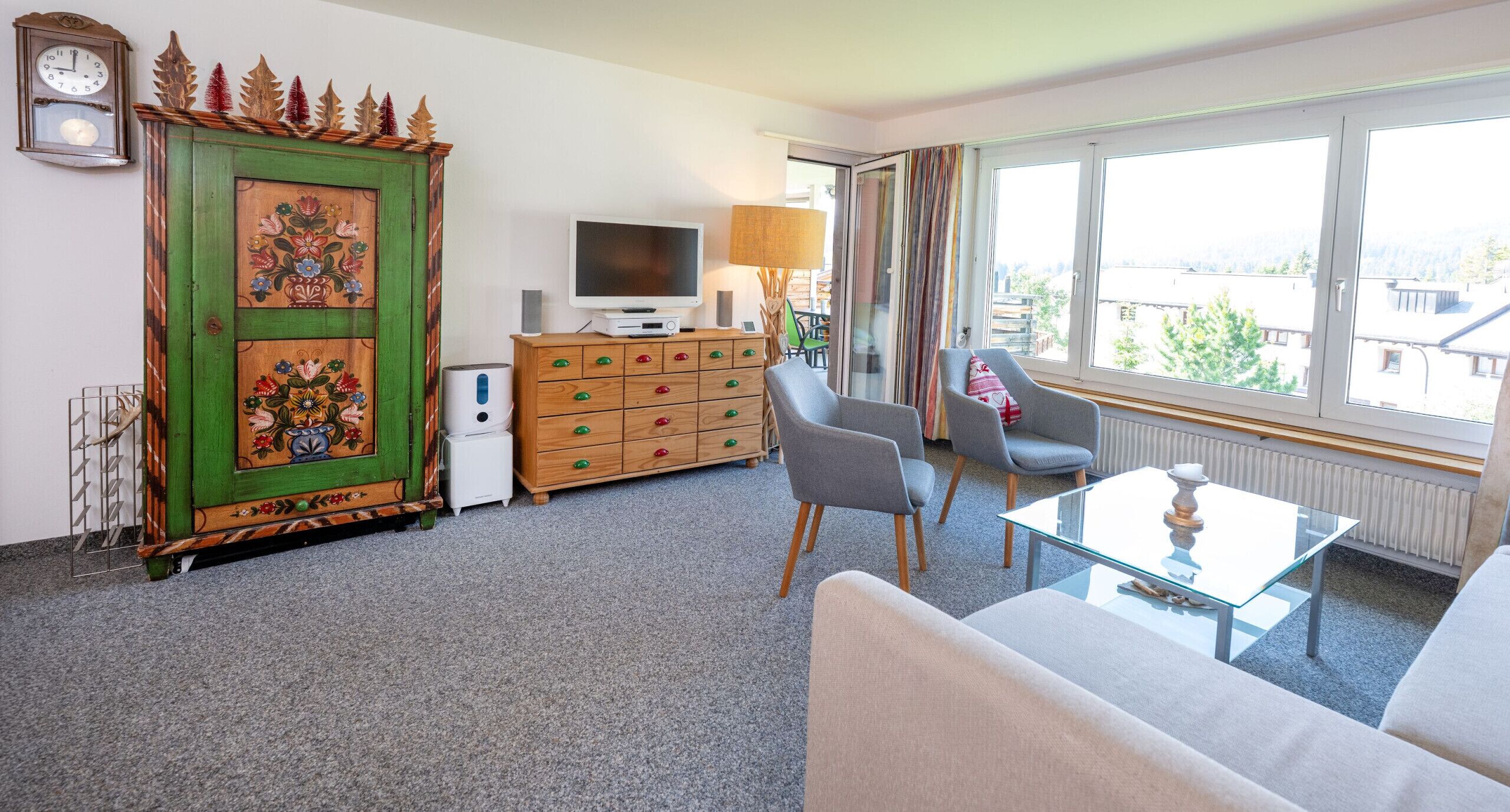 A living room with a green cabinet, a television, a sofa, and a window with a city view.