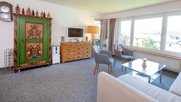 A living room with a green cabinet, a television, a sofa, and a window with a city view.