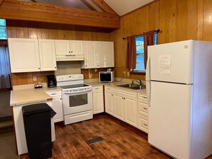 Cocina compacta con armarios blancos, estufa, microondas y refrigerador.