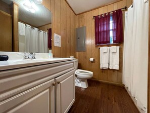 A bathroom with wooden walls, a white sink, a toilet, and a mirror. - Family-Friendly Pondside Cabin with Fountain Views Near Zwolle, Louisiana (Zwolle)