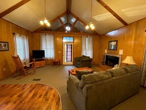 Ein gemütliches Wohnzimmer mit Kamin, Holzwänden, Fernseher und Schaukelstuhl.