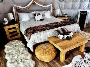 Un dormitorio con una cama con dosel, una mesita de noche de madera, una mesita auxiliar, una alfombra mullida y un banco de madera.
