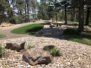 Una zona enjardinada amb un camí de grava, roques grans i un prat verd.