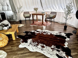 A tented room with a wooden table, two chairs, a cowhide rug, and a potted plant.