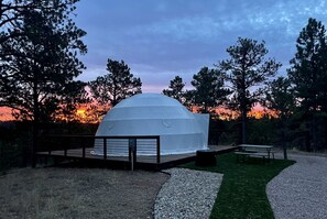 A white dome structure with a wooden deck and benches, surrounded by trees and a sunset. - Beautiful Dome with Fire Pit in Hermosa, South Dakota (Hermosa)