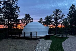 A white dome structure with a wooden deck and benches, surrounded by trees and a sunset. - Beautiful Dome with Fire Pit in Hermosa, South Dakota (Hermosa)
