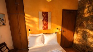 A bedroom with a wooden bed, a wall-mounted artwork, a wooden wardrobe, and a stone wall. - Diak’s Tower | Sunset Sea View in Mani (Charia)