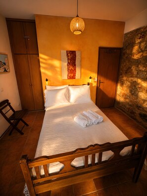Ein Schlafzimmer mit einem hölzernen Bett, einem an der Wand befestigten Kunstwerk, einem Holzschrank und einer Steinwand.