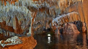 A cave interior with stalactites and stalagmites, a water body, and a light source. - Diak’s Tower | Sunset Sea View in Mani (Charia)