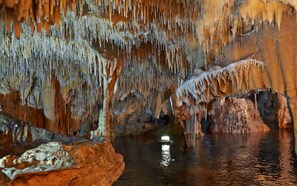 Eine Höhle mit Stalaktiten und Stalagmiten, einem Wasserspiegel und einer Lichtquelle.