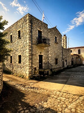 A stone building with a flag, a balcony, and a clear sky. - Diak’s Tower | Sunset Sea View in Mani (Charia)