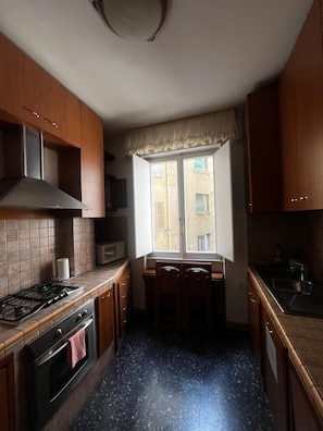 A compact kitchen with a gas stove, oven, and a window with a view of buildings outside. - Accommodation in Appia Nuova (Roma)