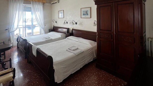 A hotel room with two beds, a wooden wardrobe, a desk, and a chair. - Accommodation in Appia Nuova (Roma)