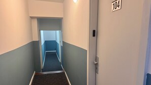 Un pasillo estrecho con piso alfombrado, una puerta con el número 104 y una lámpara en la pared.