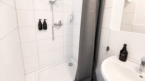 Un baño con azulejos blancos, una ducha, un lavamanos y dos botellas de jabón para manos.
