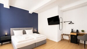 Habitación de hotel moderna con cama, mesitas de noche, escritorio, silla, televisor y una planta pequeña.