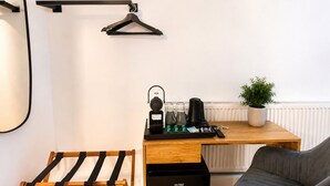 Habitación compacta con escritorio de madera, refrigerador negro, silla gris, perchero y planta en maceta.